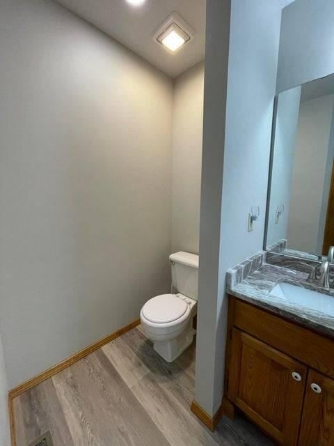 half bathroom featuring baseboards, vanity, toilet, and wood finished floors