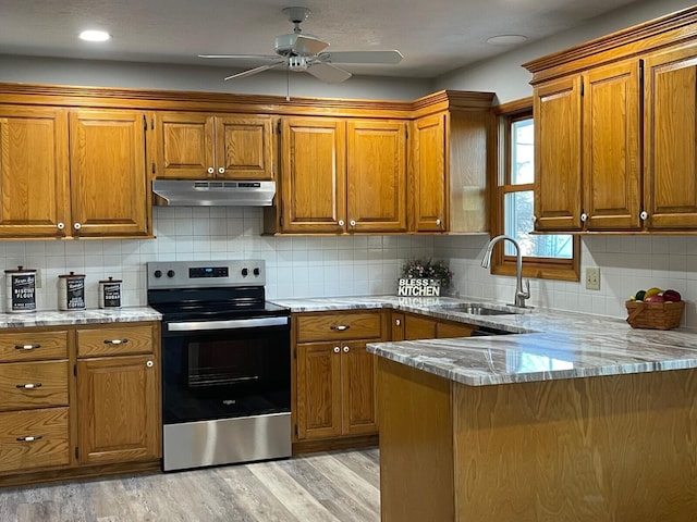 kitchen with stainless steel electric range oven, light wood-style flooring, brown cabinetry, a sink, and under cabinet range hood