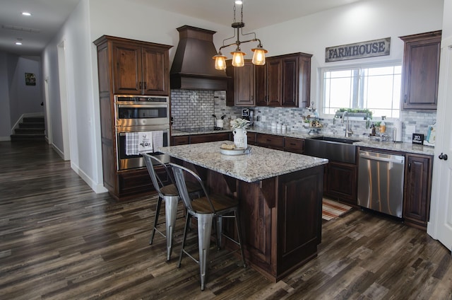 kitchen featuring dark brown cabinetry, stainless steel appliances, a kitchen island, hanging light fixtures, and custom exhaust hood