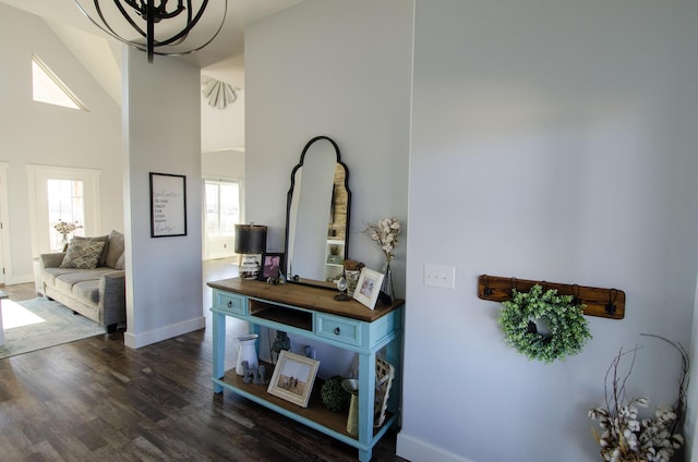 hallway with dark wood-type flooring, a towering ceiling, and baseboards