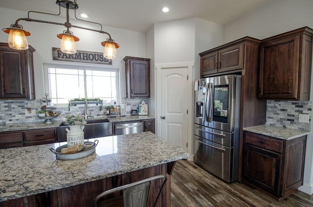 kitchen with dark brown cabinetry, appliances with stainless steel finishes, light stone counters, dark wood-type flooring, and pendant lighting