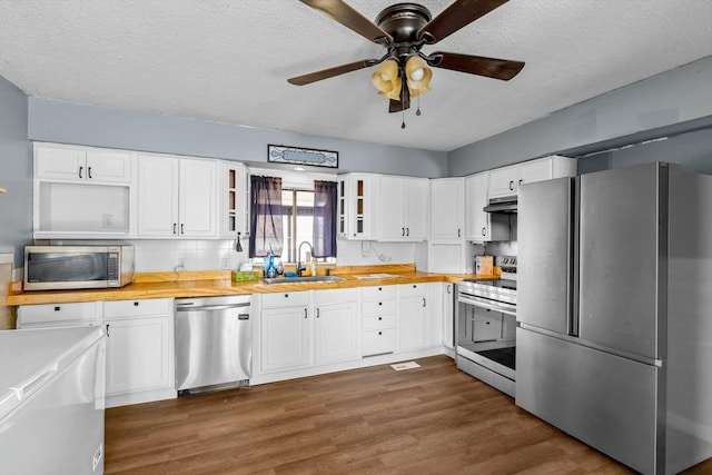 kitchen featuring appliances with stainless steel finishes, glass insert cabinets, white cabinetry, a sink, and butcher block countertops