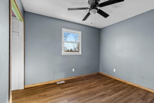 spare room with visible vents, a ceiling fan, a textured ceiling, wood finished floors, and baseboards