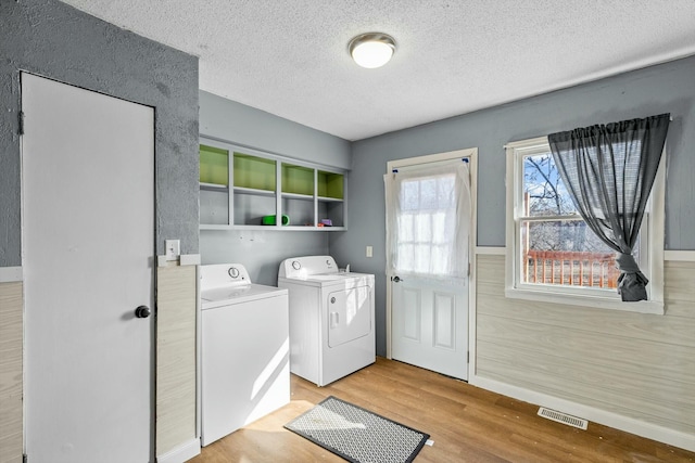 laundry room with a textured ceiling, light wood-style flooring, laundry area, visible vents, and washer and clothes dryer