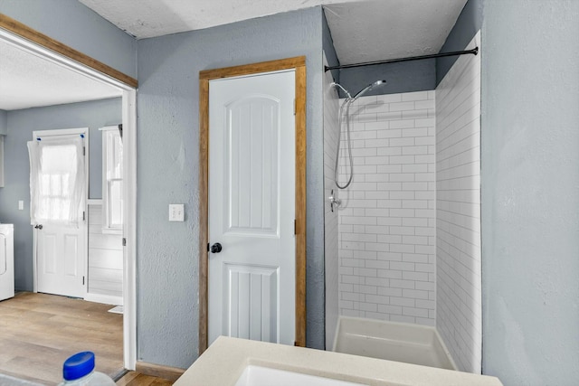 full bathroom featuring washer / clothes dryer, a textured wall, a shower stall, and wood finished floors