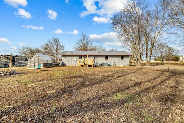 rear view of property featuring a deck, an outdoor structure, fence, a lawn, and an exterior structure