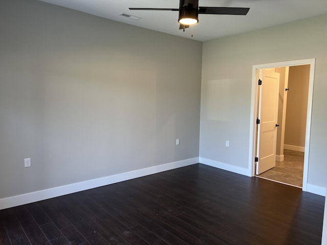 empty room featuring dark wood-style floors, a ceiling fan, visible vents, and baseboards