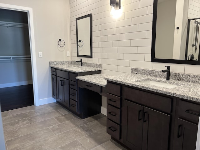 full bath featuring a sink, two vanities, baseboards, a stall shower, and a walk in closet