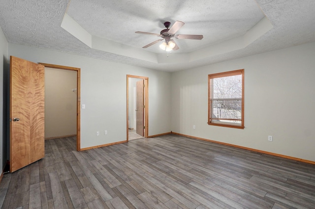 unfurnished bedroom featuring a textured ceiling, baseboards, a raised ceiling, and wood finished floors