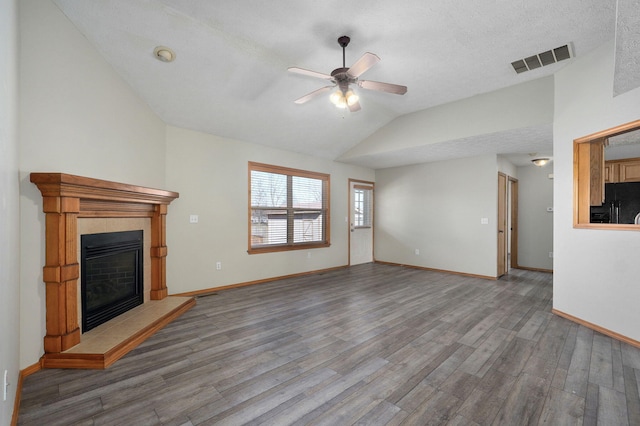 unfurnished living room with lofted ceiling, wood finished floors, visible vents, baseboards, and a tiled fireplace