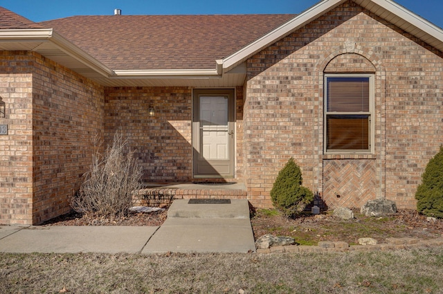 view of exterior entry with a shingled roof and brick siding