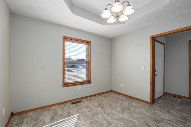 spare room featuring a tray ceiling, visible vents, a textured ceiling, a chandelier, and baseboards