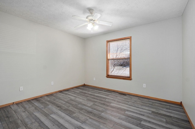 unfurnished room with a textured ceiling, wood finished floors, visible vents, and a ceiling fan