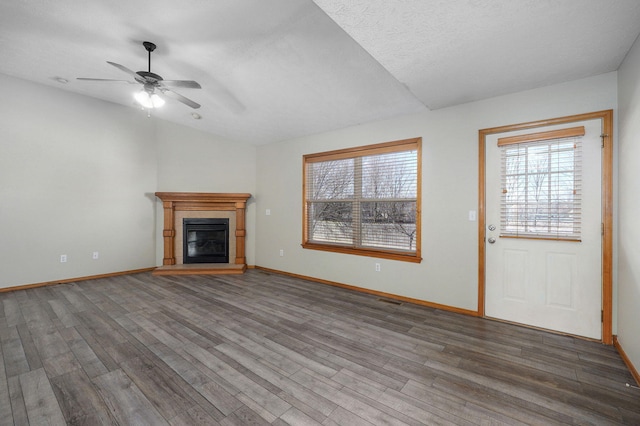 unfurnished living room with lofted ceiling, wood finished floors, a glass covered fireplace, and a healthy amount of sunlight