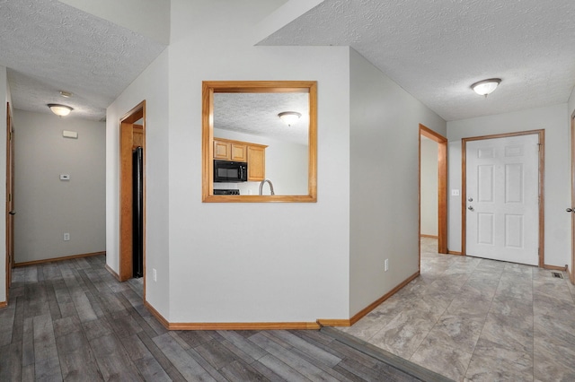 hall with light wood finished floors, baseboards, and a textured ceiling