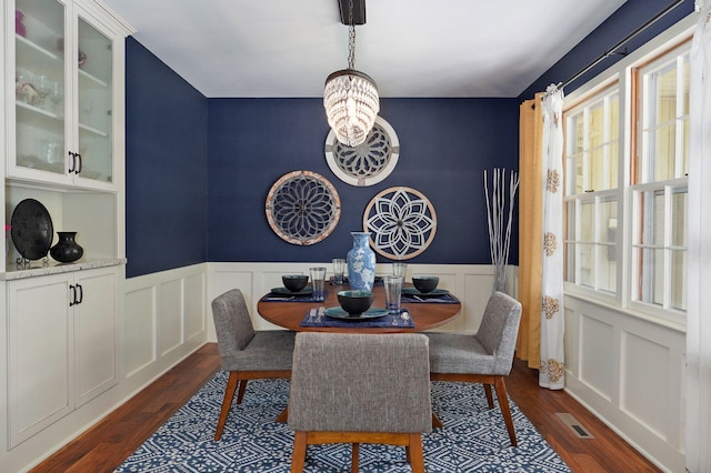 dining area with a wainscoted wall, dark wood-type flooring, visible vents, and a notable chandelier