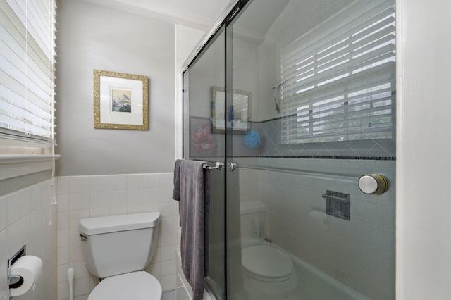 bathroom with wainscoting, a shower stall, toilet, and tile walls