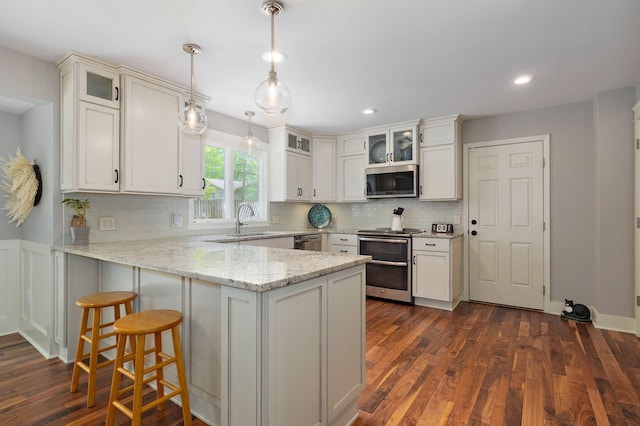 kitchen with glass insert cabinets, light stone counters, decorative light fixtures, a peninsula, and stainless steel appliances