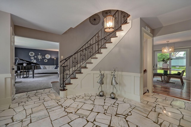 entryway with a chandelier, a wainscoted wall, a decorative wall, and stairs