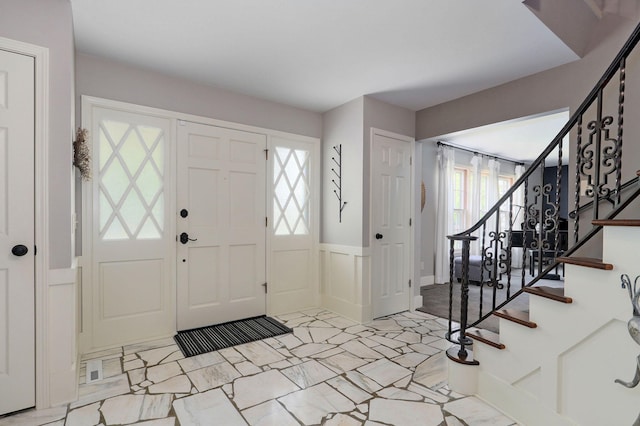 foyer featuring a wainscoted wall, plenty of natural light, a decorative wall, and stairs