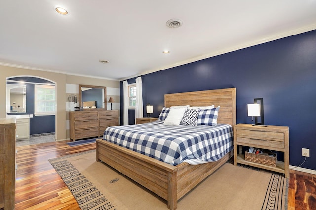 bedroom featuring crown molding, arched walkways, and wood finished floors