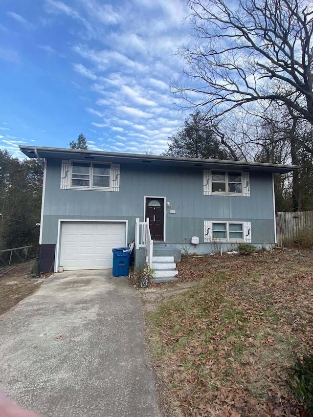 raised ranch featuring driveway, an attached garage, and fence