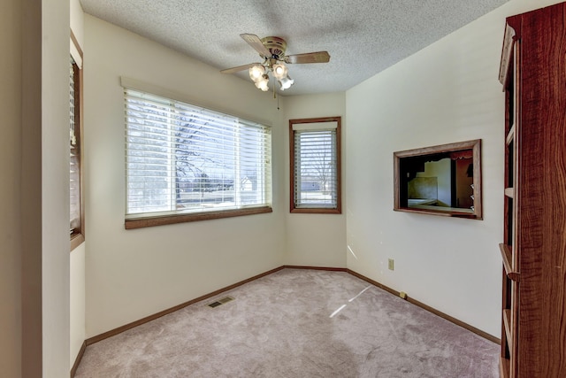 empty room with light colored carpet, visible vents, a textured ceiling, and baseboards