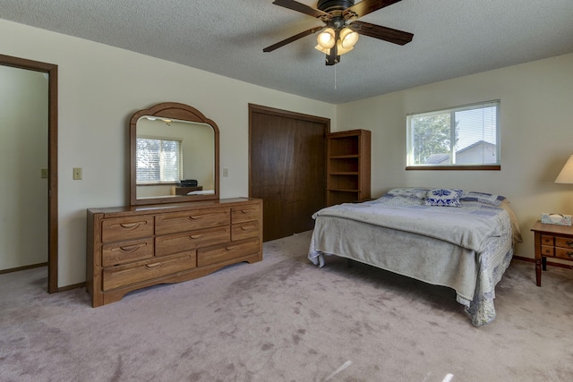 bedroom with light carpet, baseboards, a ceiling fan, a textured ceiling, and a closet