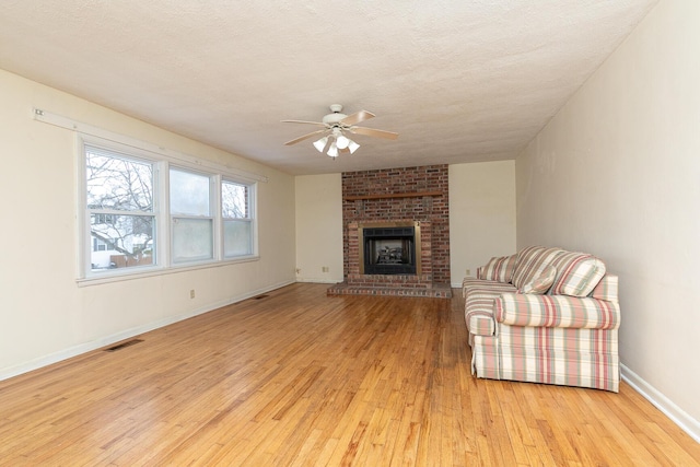 unfurnished living room featuring a brick fireplace, ceiling fan, light wood-style flooring, and a textured ceiling