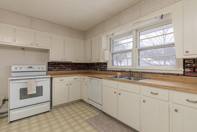 kitchen with white appliances, a sink, light floors, and wallpapered walls