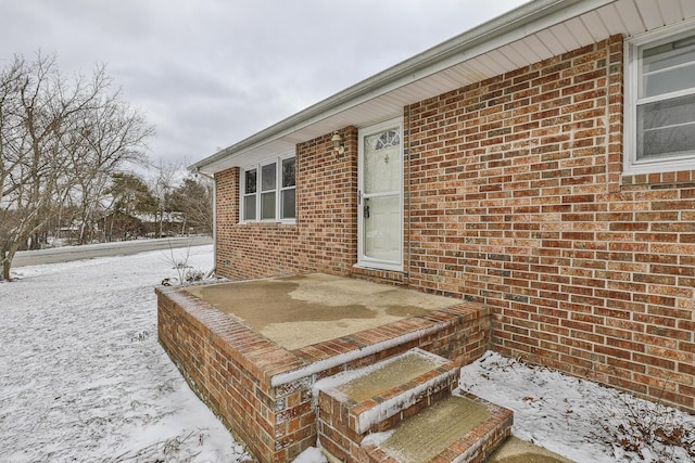 snow covered property entrance featuring brick siding