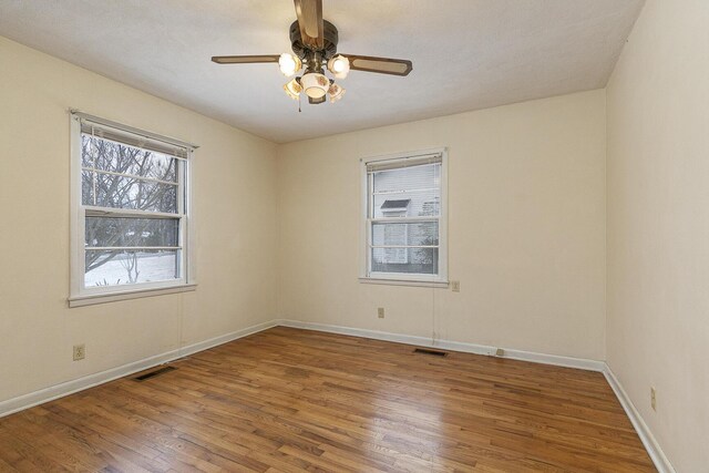 spare room featuring a ceiling fan, wood finished floors, visible vents, and baseboards