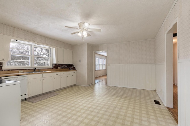 kitchen featuring wallpapered walls, visible vents, light floors, and wainscoting