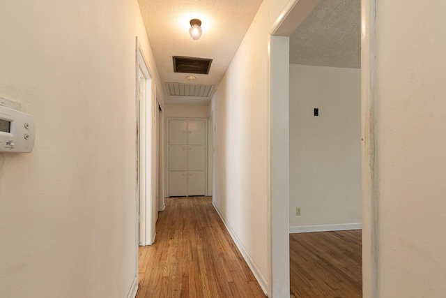 corridor with light wood-type flooring, visible vents, a textured ceiling, and baseboards