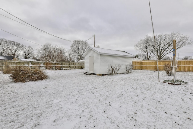 snow covered house with a fenced backyard, an outdoor structure, and a storage shed