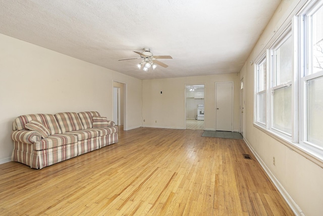 living room with a ceiling fan, baseboards, a textured ceiling, and light wood finished floors