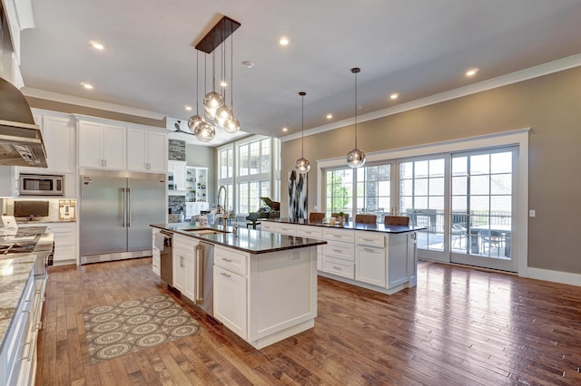 kitchen with an island with sink, a sink, white cabinetry, wood-type flooring, and built in appliances