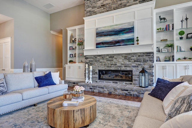 living area featuring a glass covered fireplace, built in shelves, visible vents, and wood finished floors