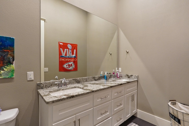 bathroom featuring double vanity, toilet, baseboards, and a sink