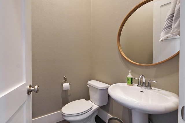 half bathroom featuring toilet, a textured wall, and a sink