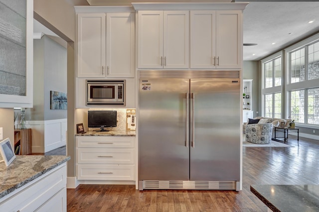 kitchen featuring built in appliances, hardwood / wood-style flooring, white cabinets, and light stone countertops