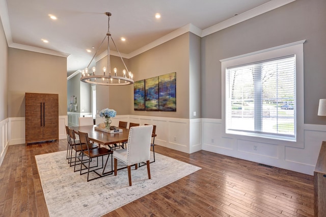 dining area featuring dark wood-type flooring, ornamental molding, a wainscoted wall, and a chandelier