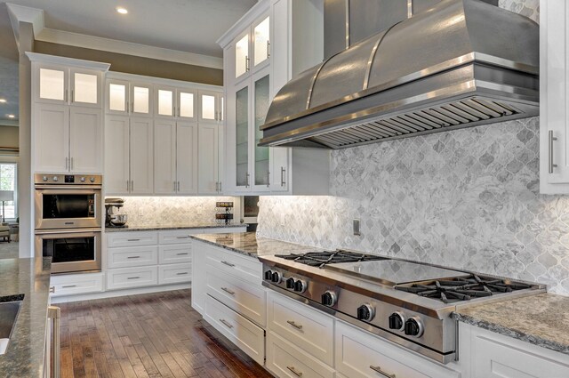 kitchen with light stone counters, stainless steel appliances, extractor fan, and white cabinetry