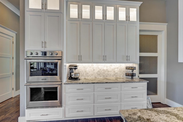 kitchen featuring stainless steel double oven, tasteful backsplash, white cabinets, and dark wood finished floors