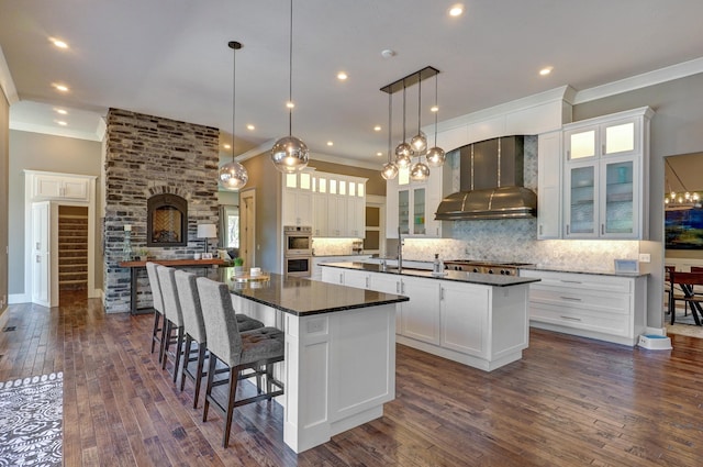 kitchen featuring stainless steel appliances, a large island, dark countertops, and wall chimney exhaust hood