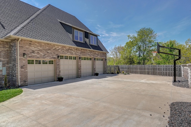 view of side of home with fence, concrete driveway, an attached garage, a shingled roof, and brick siding