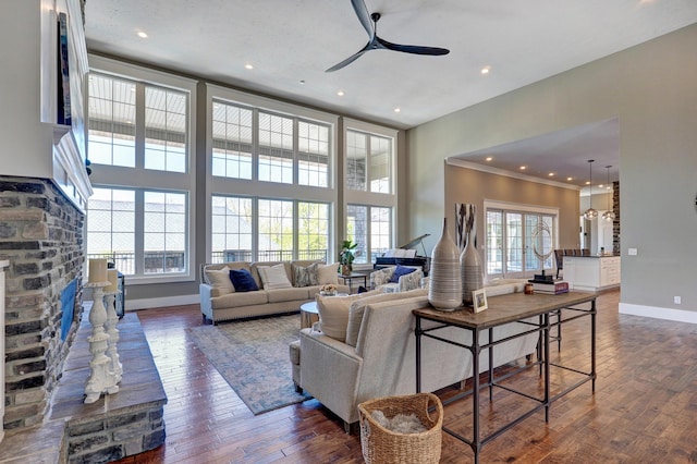 living room featuring baseboards, a fireplace, ceiling fan, dark wood-type flooring, and a towering ceiling