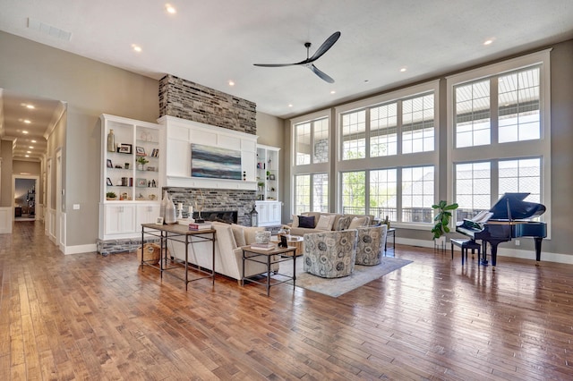 living area with a brick fireplace, a towering ceiling, visible vents, and wood-type flooring