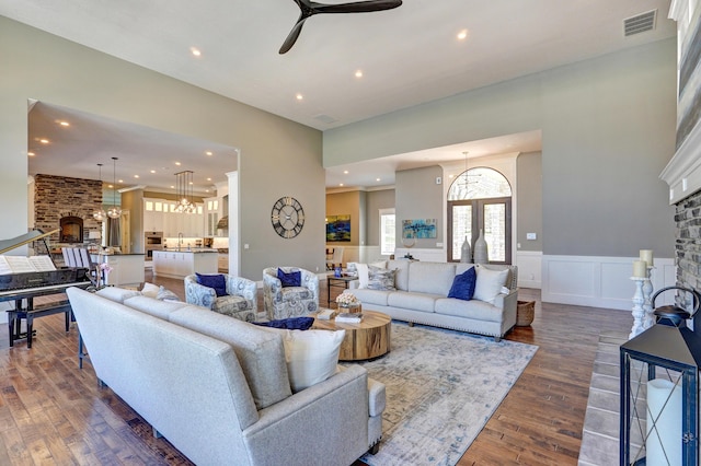 living room featuring a wainscoted wall, visible vents, a fireplace, dark wood-type flooring, and ceiling fan with notable chandelier