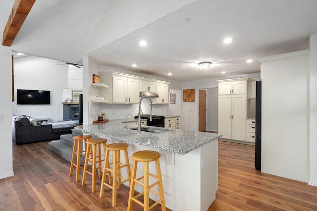 kitchen featuring a breakfast bar area, dark wood-type flooring, white cabinets, ceiling fan, and light stone countertops